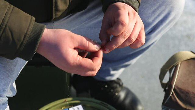 The fisherman puts the bait on a jig hook to fish under the ice in winter. Scene of winter ice fishing with tackle