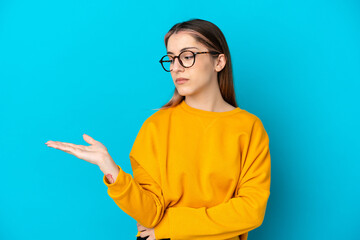 Young caucasian woman isolated on blue background holding copyspace with doubts