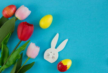 Pink and red tulips, Easter eggs, and a wooden bunny on a blue background. Background for design. Spring background. Mother's Day. Women's Day. Spring day. Easter background. Easter. Copy space.