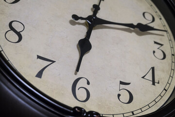 Detail of classic vintage round mechanical wall clock with black clock hands and numbers. Limited depth of field.