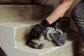 Grinding concrete staircase surfaces with an electric sander. Worker woman with hand tool grinding machine.