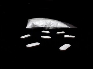 Cocaine drug powder in bag and pills on black background