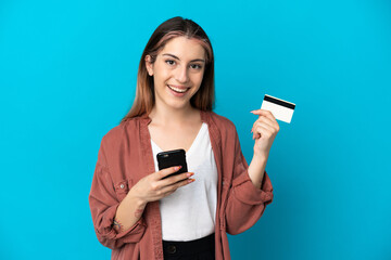 Young caucasian woman isolated on blue background buying with the mobile and holding a credit card with surprised expression