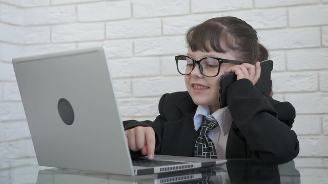 Child dialing. A nice happy child in a suit play like a boss and speak on telephone and work on computer in the office.