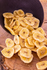 Banana chips spilling out of a dark ceramic cup on a wooden background