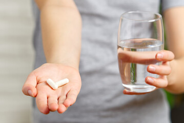 girl hand with white pills medicine tablets and glass of water