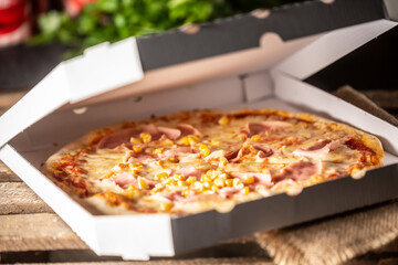 Pizza with ham, corn and cheese in a half-open white pizza box