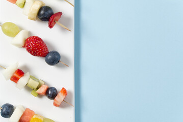 Naklejka na ściany i meble fresh summer fruit snacks on bamboo skewers, isolated on blue