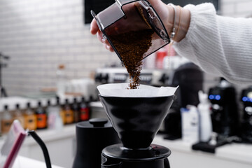 Making filter coffee. Add coffee. Hand with coffee over natural interior.