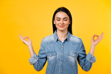 Photo of a pretty caucasian positive young woman with closed eyes, meditates and smiles on isolated orange color background