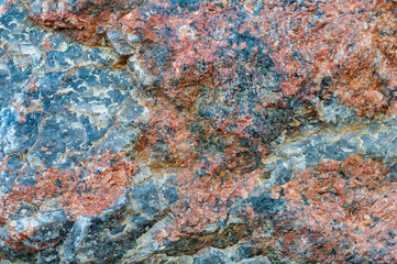 Chipped red gray granite stone close-up, beautiful texture, rough textured surface, exposure to atmosphere, outdoors.
