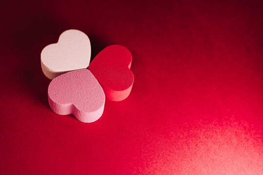 Top view of a three little hearts of sponges on a red background. There are one white heart, one pink heart and one red heart situated together. San Valentine's day backgrounds concept