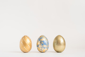 Three Easter golden decorated eggs on white background. Minimal easter concept. Happy Easter card with copy space for text. Top view, flatlay.