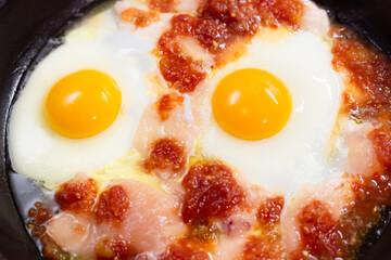 Omelet frying. Fried eggs with chicken in tomato paste. Egg yolks on a frying pan