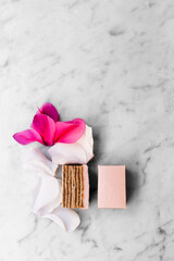 Pink cake and flower petals on white marble background.