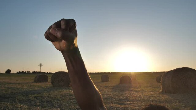 Close-up of raised black male fist symbolizing protest against racism, discrimination and fight for civil rights, equality. Dark-skinned man raising clenched fist on background of setting sun