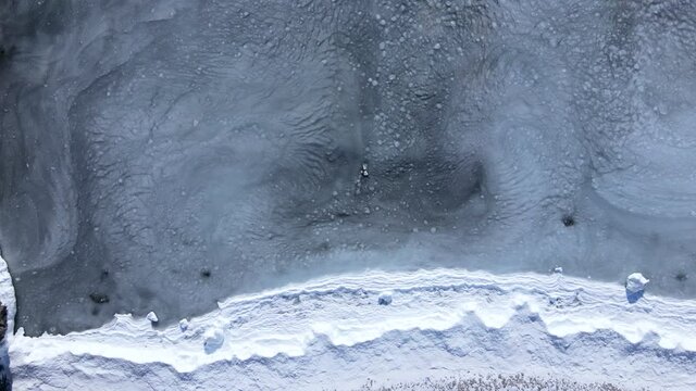 Snowy coast. View from above. The camera hovers over the snowy coast and the sea with sludge rolling onto the shore