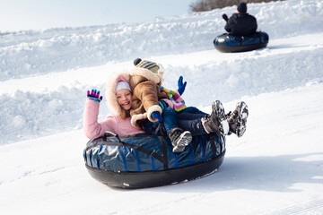 a boy and a girl ride a tubing downhill