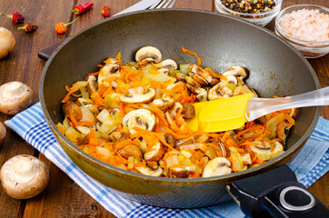Frying pan with fried mushrooms champignons, onions and carrots on wooden background. Studio Photo
