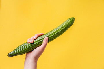Female hand holding cucumber on yellow background - Woman hold green cucumber with copy space -...