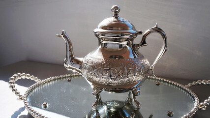 Moroccan metallic teapot on a silver tray in broad daylight, closeup