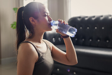 Young fit attractive Asian woman drinking water after workout at home.