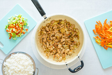 Fried chopped meat on frying pan, boiled rice in colander and chopped vegetables on cutting boards, close up view, flat lay