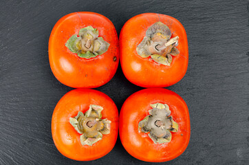 Sweet juicy orange persimmon on contrasting black background. Studio Photo