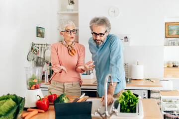 Senior couple preparing healthy smoothie in kitchen and using tablet to read recipe