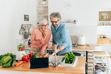 Senior couple preparing healthy smoothie in kitchen and using tablet to read recipe