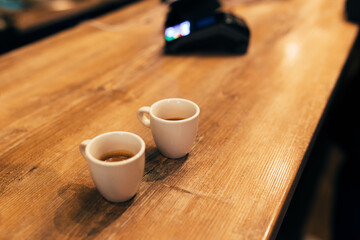 Two cups of espresso coffee at table in cafe, bank terminal. Blurred background