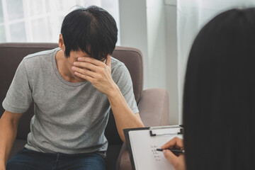 Young asian man, male has mental symptoms which must have been therapy and stress, sitting on couch...