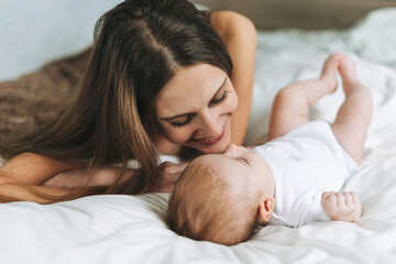 Young mother having fun with cute baby girl on bed, love emotion