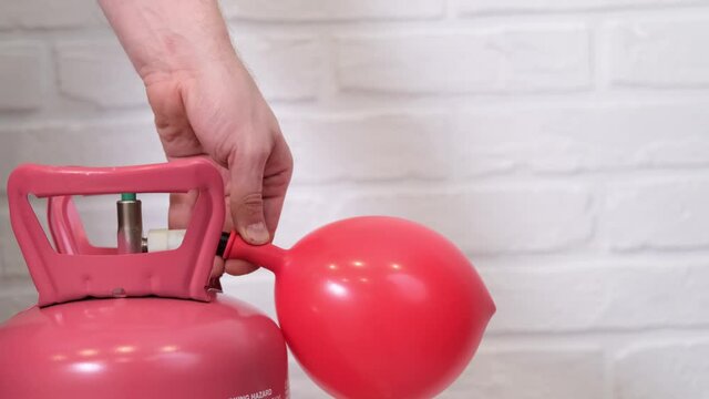 Man hand inflating red heart shaped balloon with helium from balloon. Preparation for holiday Valentines Day, room decoration slow motion