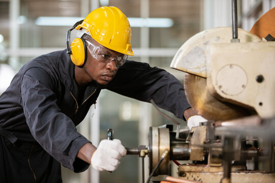 Black male african american workers wear sound proof headphones and yellow helmet working an iron cutting machine in factory Industrial.