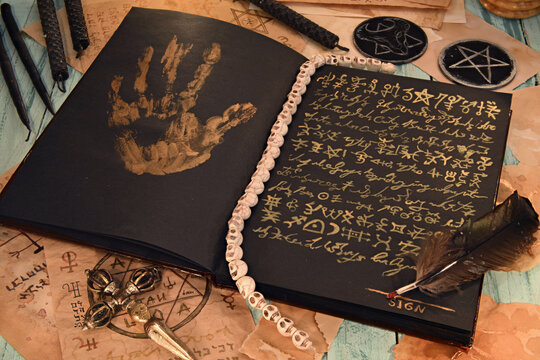 Open grimoire book of magic spells with black candles on witch table, sell soul to the devil concept.