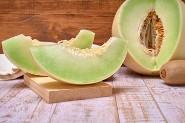 green melon sliced on wooden board with kiwis and a half melon . over a wooden table and wooden background. healthy food concept. Summer fruit