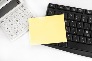 A blank yellow sheet lies on a white calculator and a black keyboard. The concept of online learning and business.