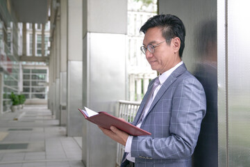 Businessman leaning against building pillar and looking at his diary