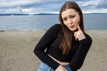 Fototapeta na wymiar Teenage girl outside at Alki Beach in West Seattle with a view of the Puget Sound and the city of Seattle in Washington State. 