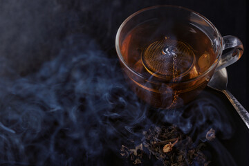 Hot tea in a clear glass with smoke on the table and a black background.