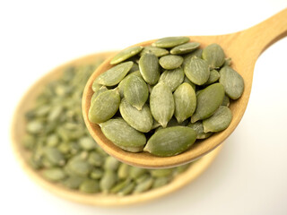Closeup organic pumpkin seeds in wooden spoon and heap pumpkin seeds on wooden plate isolated top view on white background for pumpkin seeds can improve health concept.