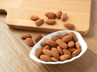 Organic almonds nuts in ceramic bowl with wooden butcher on wooden table. Set or collection for healthy nuts and vegetarian food concept.