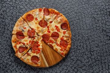 Pepperoni pizza, on a black textured background. Italian food concept. Close-up.