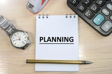 The word planning is written in a notebook that lies on a wooden table. Calculator and wristwatch. Business concept