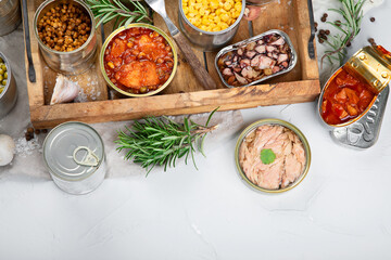 Various canned vegetables, fish and peas in aluminum cans on light gray background.