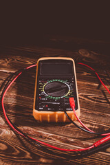 Multimeter and two test leads on a wooden background. A studio photo with hard lighting.