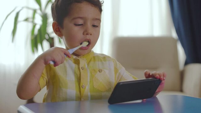 Boy brushing his teeth while watching cartoons on the phone.