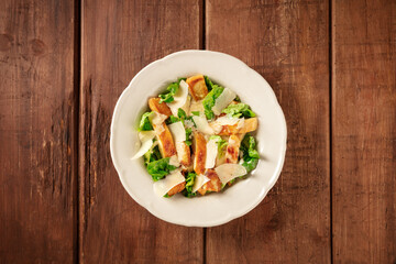 Caesar salad with grilled chicken, romaine and Parmesan cheese, shot from above on a dark rustic wooden background