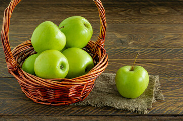 Organic Granny Smith apples in a wicker basket on wooden table